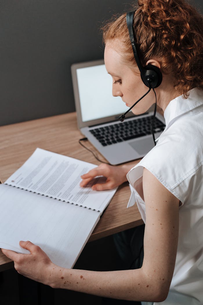 A woman wearing a headset studies a document at her work desk indoors.